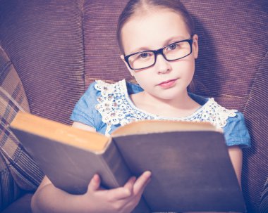 Kız evde kitap okurken bir koltukta oturan.