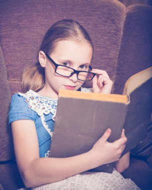 Kız evde kitap okurken bir koltukta oturan.