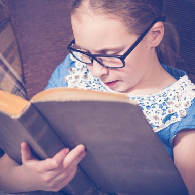 Kız evde kitap okurken bir koltukta oturan.