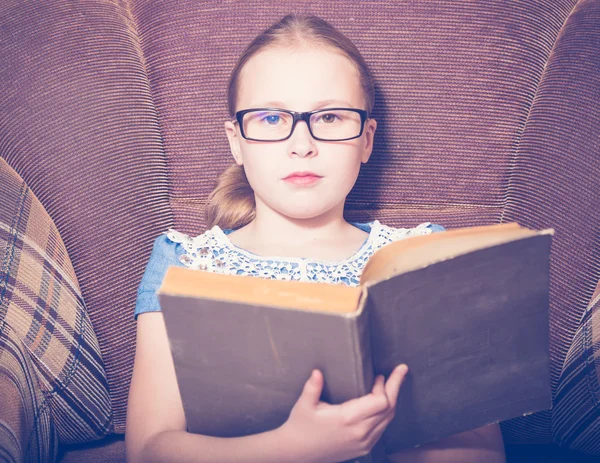 Kız evde kitap okurken bir koltukta oturan. — Stok fotoğraf