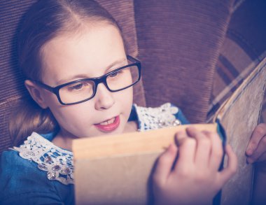 Kız evde kitap okurken bir koltukta oturan.