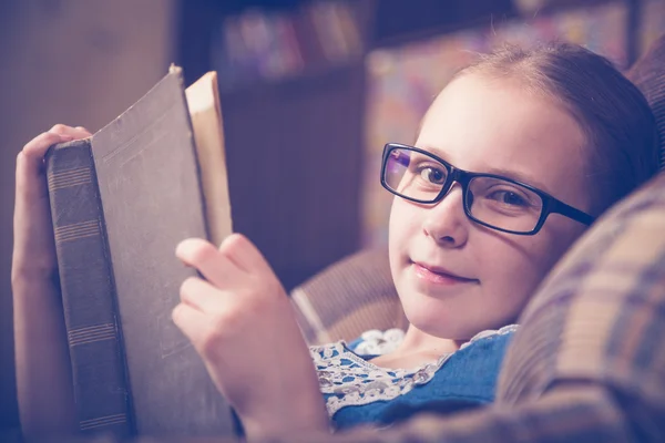 Kız evde kitap okurken bir koltukta oturan. — Stok fotoğraf
