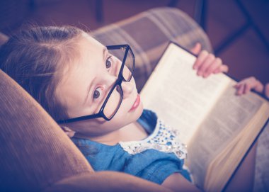 Kız evde kitap okurken bir koltukta oturan.