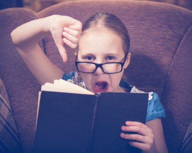 Kız evde kitap okurken bir koltukta oturan.