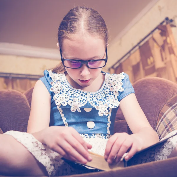 Meisje het lezen van een boek thuis zitten in een leunstoel. — Stockfoto