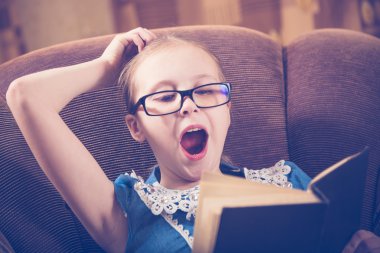 Kız evde kitap okurken bir koltukta oturan.