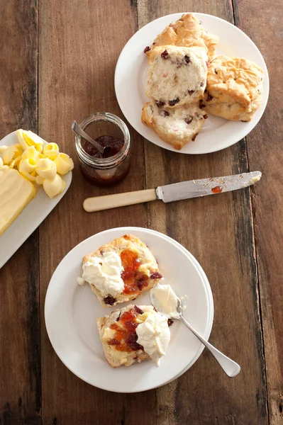 焼きたてのフルーティーなロックケーキやレーズンパンにジャムとホイップクリームを添えて バターのパットと一緒に木製のテーブルの上から見渡します — ストック写真