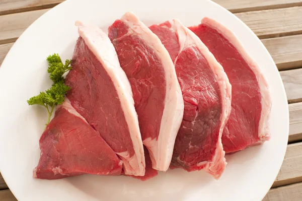 Чотири свіжих сирих яловичих стейки на тарілці — стокове фото