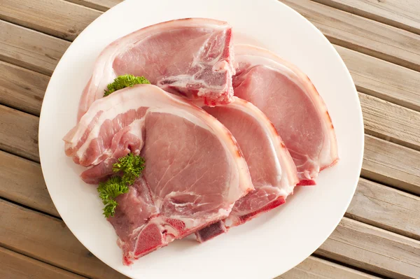 Four raw pork cutlets on a plate — Stock Photo, Image