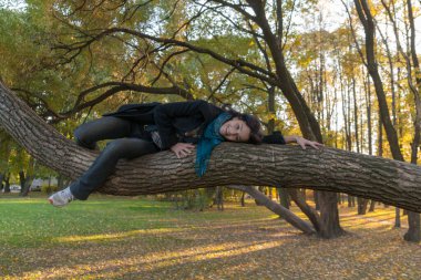 Sonbahar parkında ağaç gövdesinde bir kızın portresi.