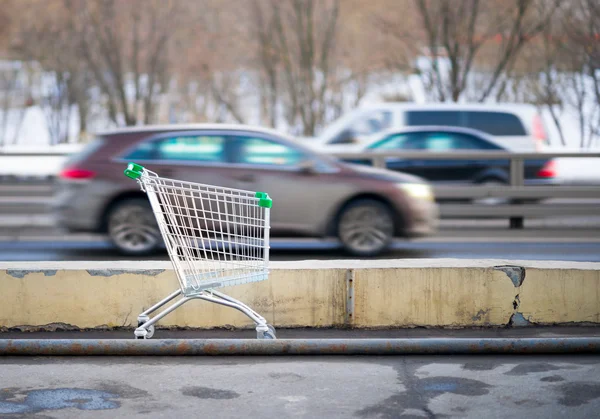 Shopping cart on background rushing cars — Stock Photo, Image