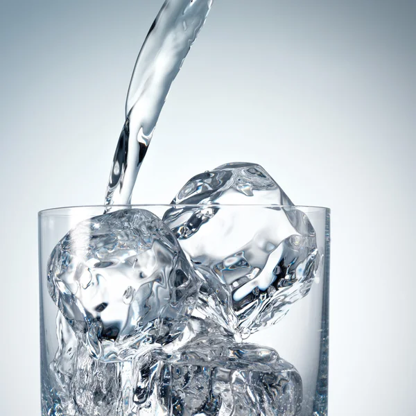 Gieten van water in een glas met ijs — Stockfoto