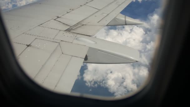 Grond en wolken onder vleugels van een vliegtuig tijdens de vlucht — Stockvideo