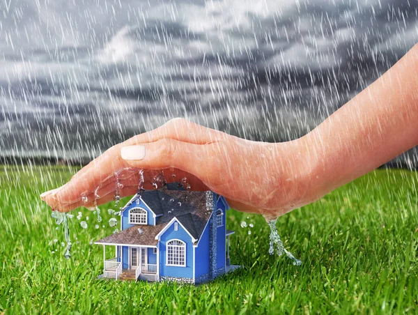 Save house. Hand protecting house from rain on a overcast weather background.