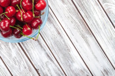 cherries in a glass bowl on a white wooden background