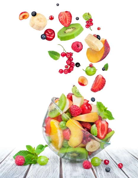 Obstsalat in Glasschüssel mit Zutaten in der Luft auf weißem — Stockfoto