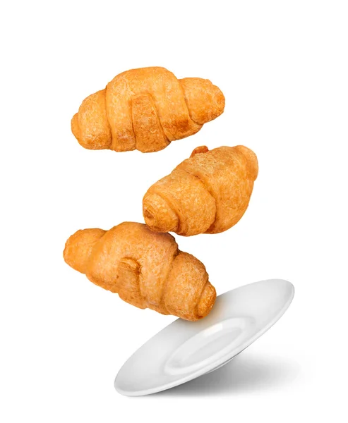 Three falling croissant and white saucer isolated on white backg — Stock Photo, Image