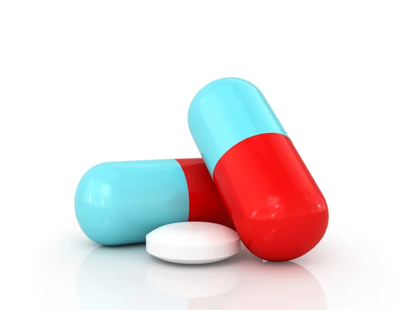 Dos píldoras de colores y tableta blanca sobre un fondo blanco — Foto de Stock