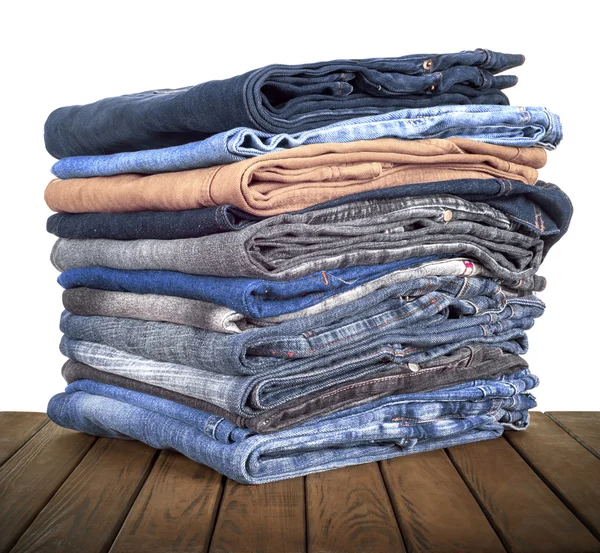 Pilha de jeans deitada em uma mesa de madeira — Fotografia de Stock