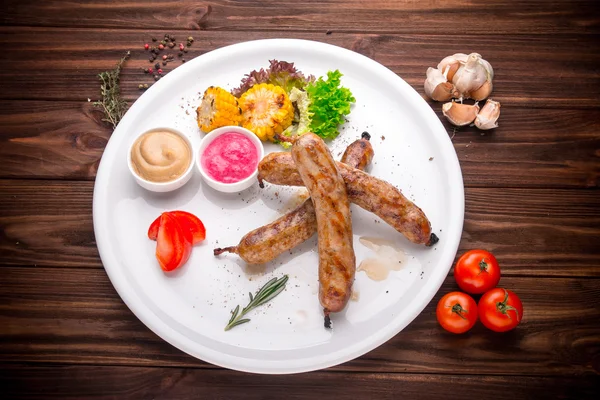 Grilled sausages with vegetables and seasoning on wood — Stock Photo, Image