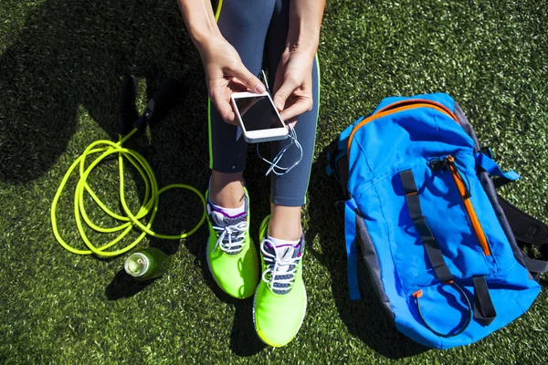 Gree üzerinde oturan boş ekranlı telefonu tutan sportif kadın — Stok fotoğraf