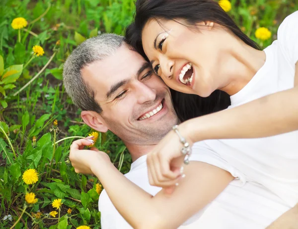 Jeune couple amoureux couché sur l'herbe verte avec pissenlit — Photo