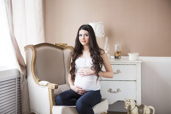 Mujer embarazada sentada en sillón en habitación acogedora —  Fotos de Stock