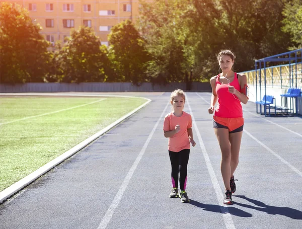 Mother and little daughter are doing exercise in the stadium. He — Stock Photo, Image