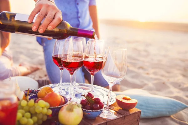 Amici felici che bevono vino rosso sulla spiaggia. Festa al tramonto sulla spiaggia — Foto Stock