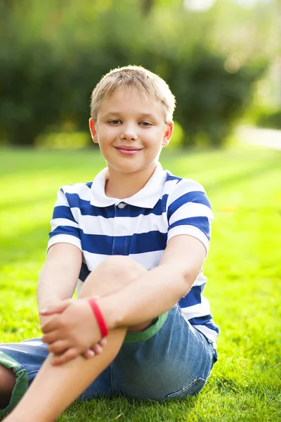 Liten pojke sitter på gräset med leende — Stockfoto