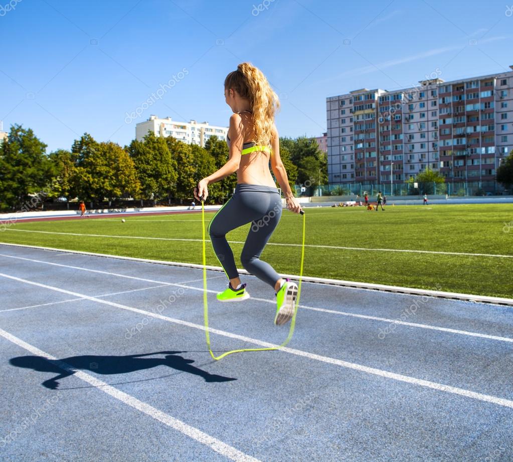 Jovem mulher com uma corda de salto nas mãos com um estádio como b — Fotografia de Stock