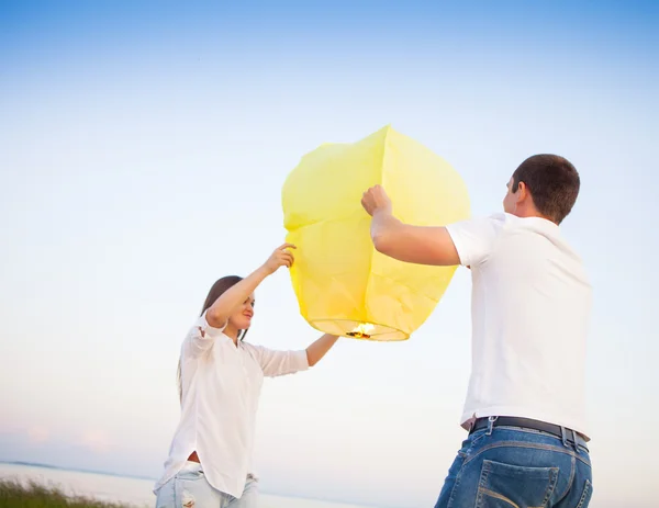 Young couple start a yellow Chinese sky lantern near the sea — Stock Photo, Image