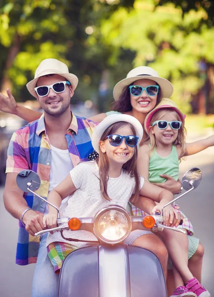 Heureuse jeune famille chevauchant un scooter vintage dans la rue wearin — Photo