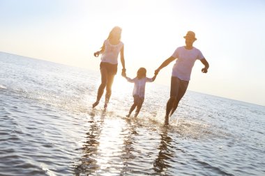 Mutlu genç aile eğleniyor kumsalda günbatımında çalışan