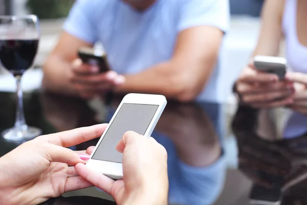 Tre vänner med smarta telefoner hålla glas med rött vin — Stockfoto