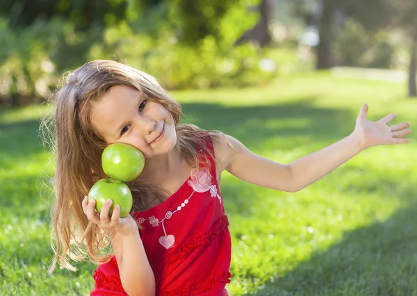 Ragazzina divertente con mele verdi nel parco estivo — Foto Stock