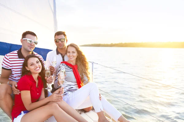 Улыбающиеся друзья, сидящие на палубе яхты и приветствующие выпивоху — стоковое фото