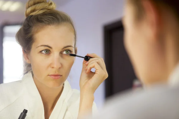 Mujer aplicando maquillaje mirando el espejo — Foto de Stock