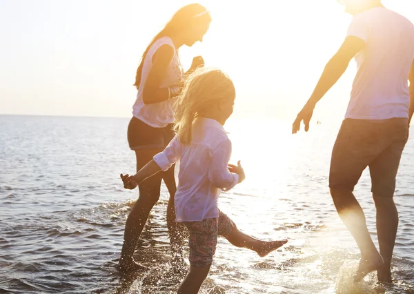 Счастливая молодая семья весело бегает по пляжу на закате — стоковое фото