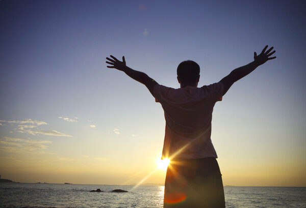 Silhouette of a man raising his hands or open arms on the beach 