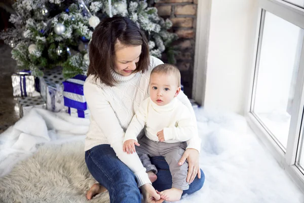 Madre con su bebé sentado cerca del árbol de Navidad — Foto de Stock