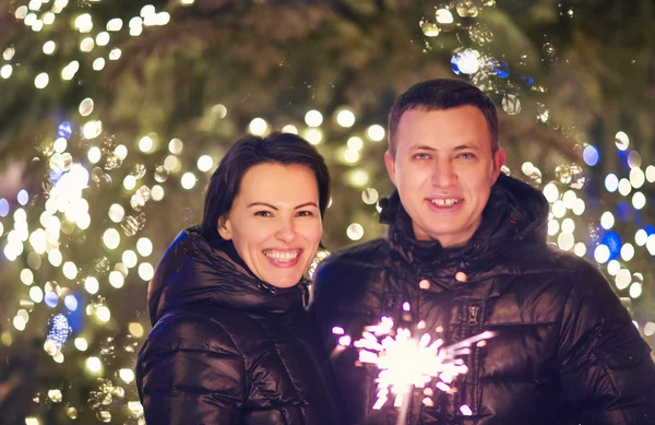 Pareja con luz de Bengala mirando a la cámara exterior sobre Christma —  Fotos de Stock