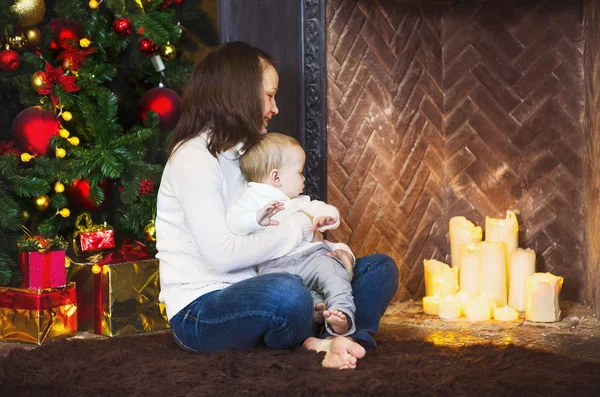 Madre con su bebé sentado cerca del árbol de Navidad — Foto de Stock