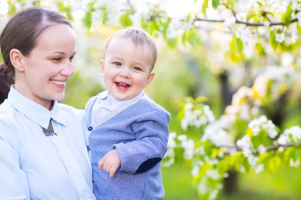 Baby jongetje met jonge moeder in de bloeiende tuin — Stockfoto