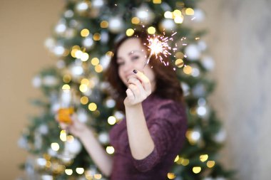 Işıl ışıl parlayan yılbaşı ağacının karşısında duran parlak maytap ve bir kadeh şampanyayla neşeli genç bayanın yumuşak odağı.