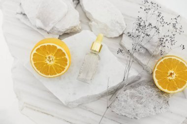 Masada taş ve olgun portakallarla sıralanmış yüz serumlu cam şişe.