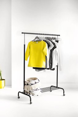 Beyaz duvarlı, minimalist tarzda bir odaya yerleştirilmiş çeşitli kadınsı gömlekli raflar.