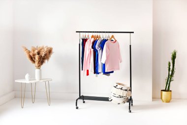 Beyaz duvarlı, minimalist tarzda bir odaya yerleştirilmiş çeşitli kadınsı gömlekli raflar.