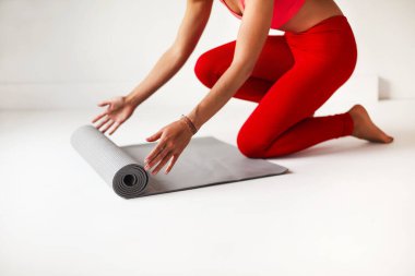 Beyaz stüdyoda yoga çalışması için parlak kırmızı tişörtlü, deri ceketli, kimliği belirsiz, zayıf bir kadının yan görüntüsü.