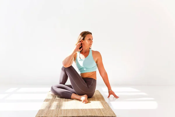 穿着运动服 一边练习瑜伽 一边在垫子上保持平衡 一边望着别处的冷静女性的侧面视角 — 图库照片